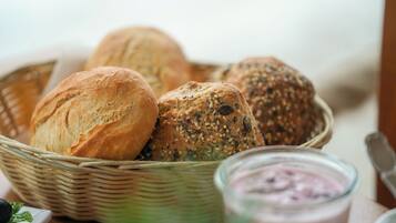Een mand met verschillende broden, waaronder volkoren en zadenbrood, op een houten tafel.