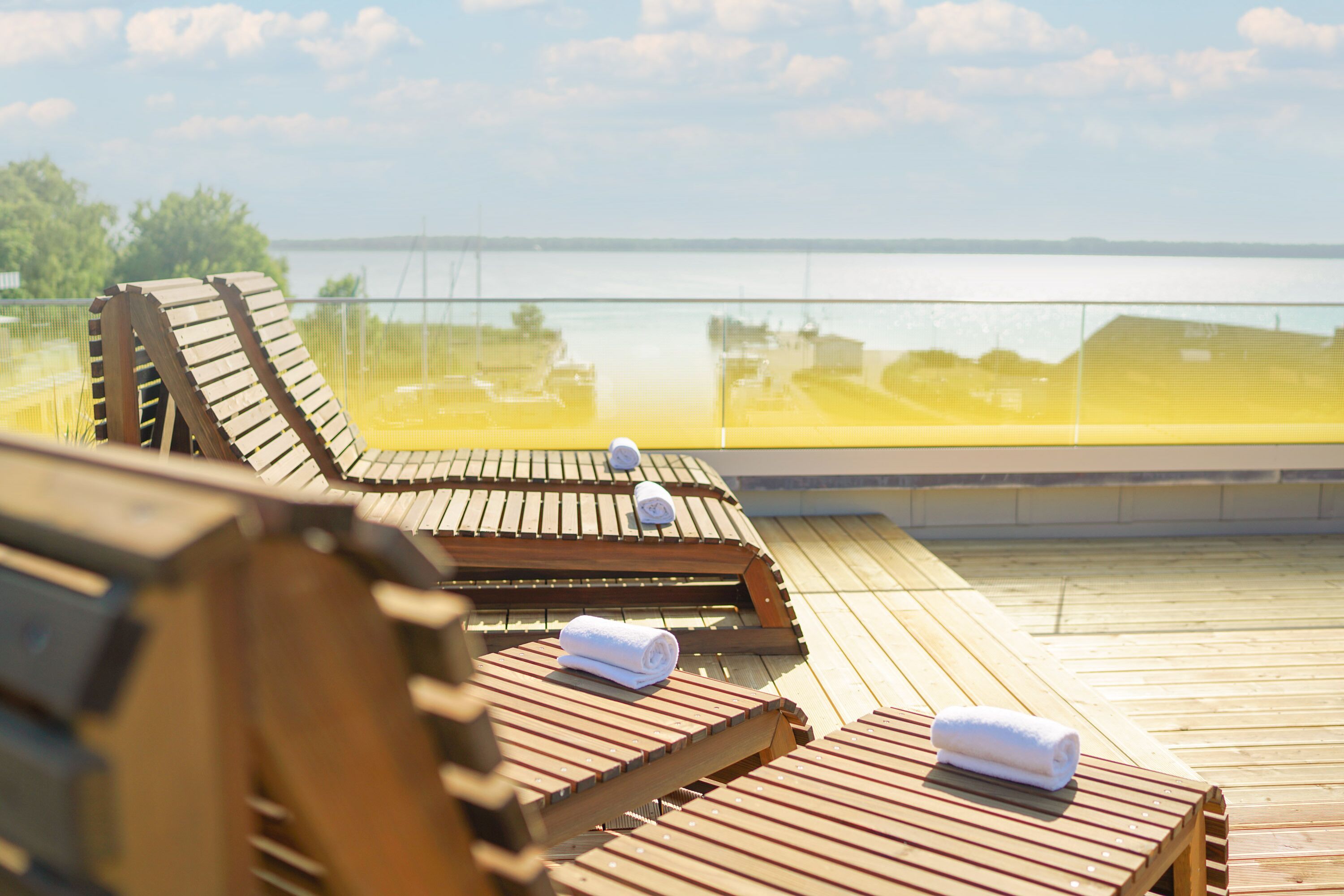 A wooden deck with lounge chairs and towels, overlooking a body of water.
