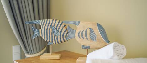 A wooden fish-shaped decoration on a wooden table in a room with a curtain and a white pillow.