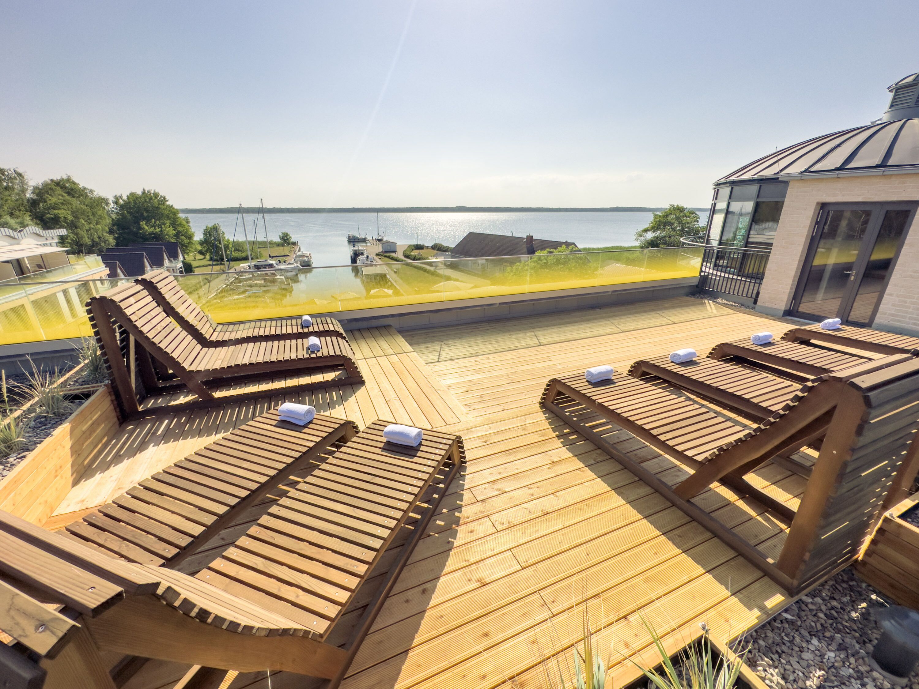 A wooden deck with lounge chairs and a glass balustrade overlooking a body of water.