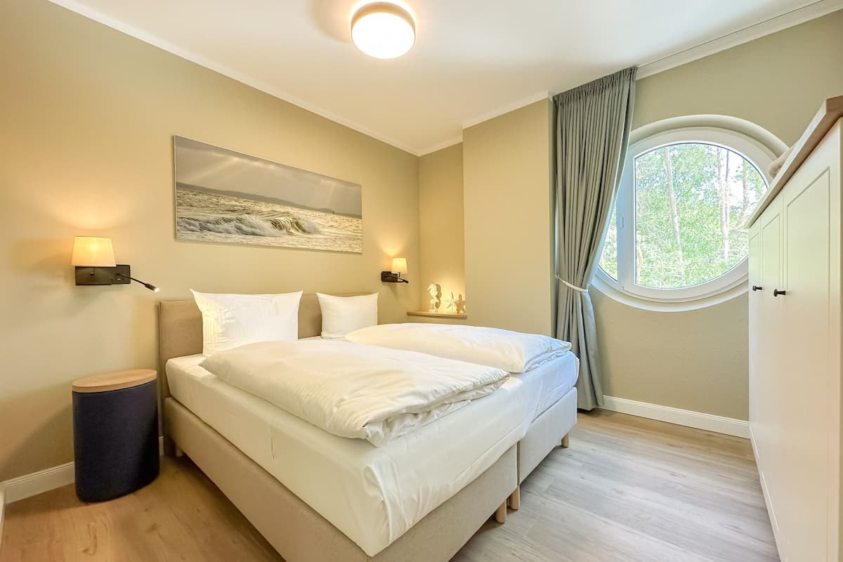 Una camera da letto con un letto grande, due lampade sui comodini, un quadro, una finestra con tende e una plafoniera a forma di cerchio.
