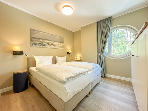 A bedroom with a large bed, two bedside lamps, a painting, a window with curtains, and a round ceiling light. - Appartements Zum Leuchtturm (Rankwitz)