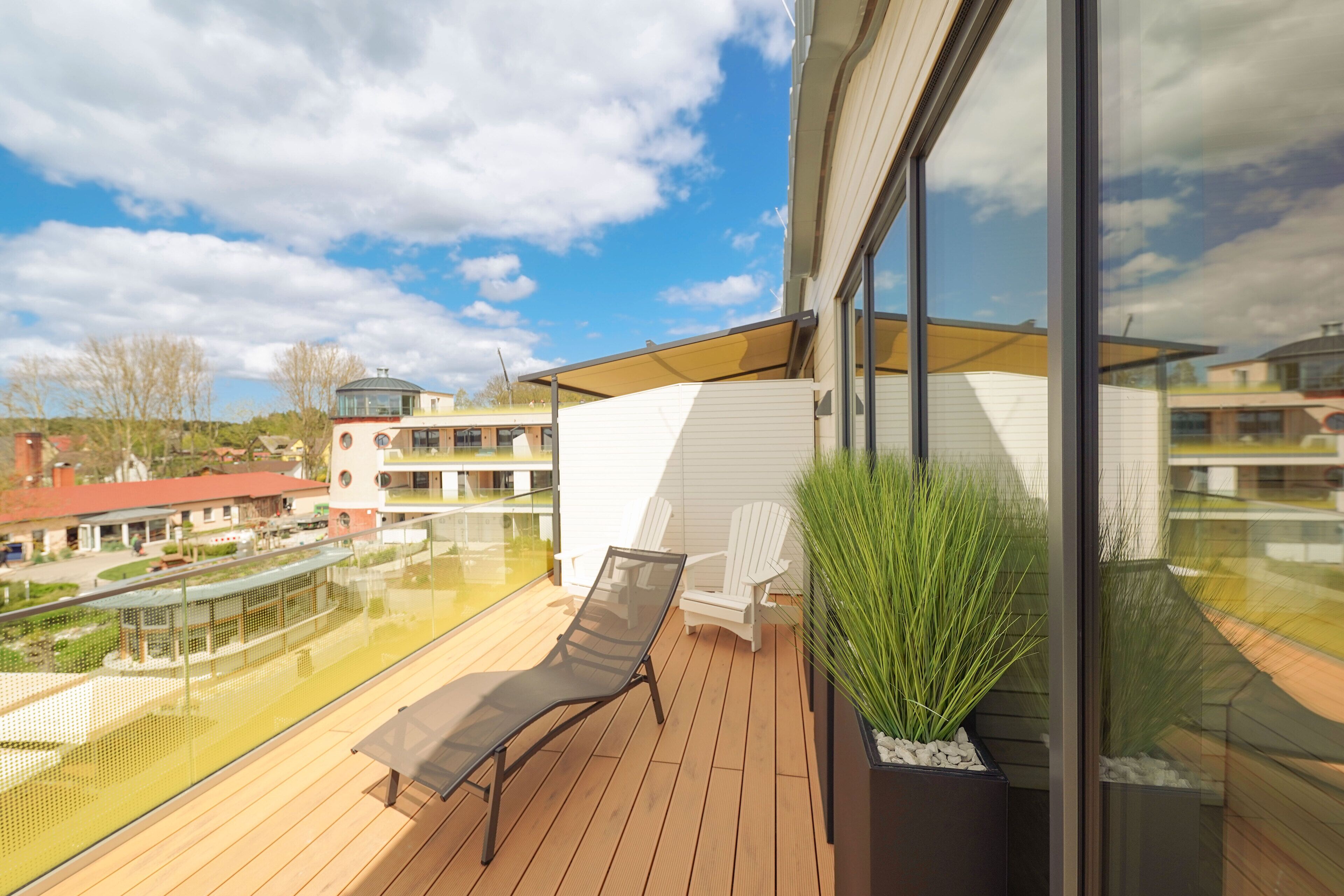 Un balcon doté d’un plancher en bois, d’un fauteuil de relaxation, d’une plante en pot et d’une rambarde en verre.