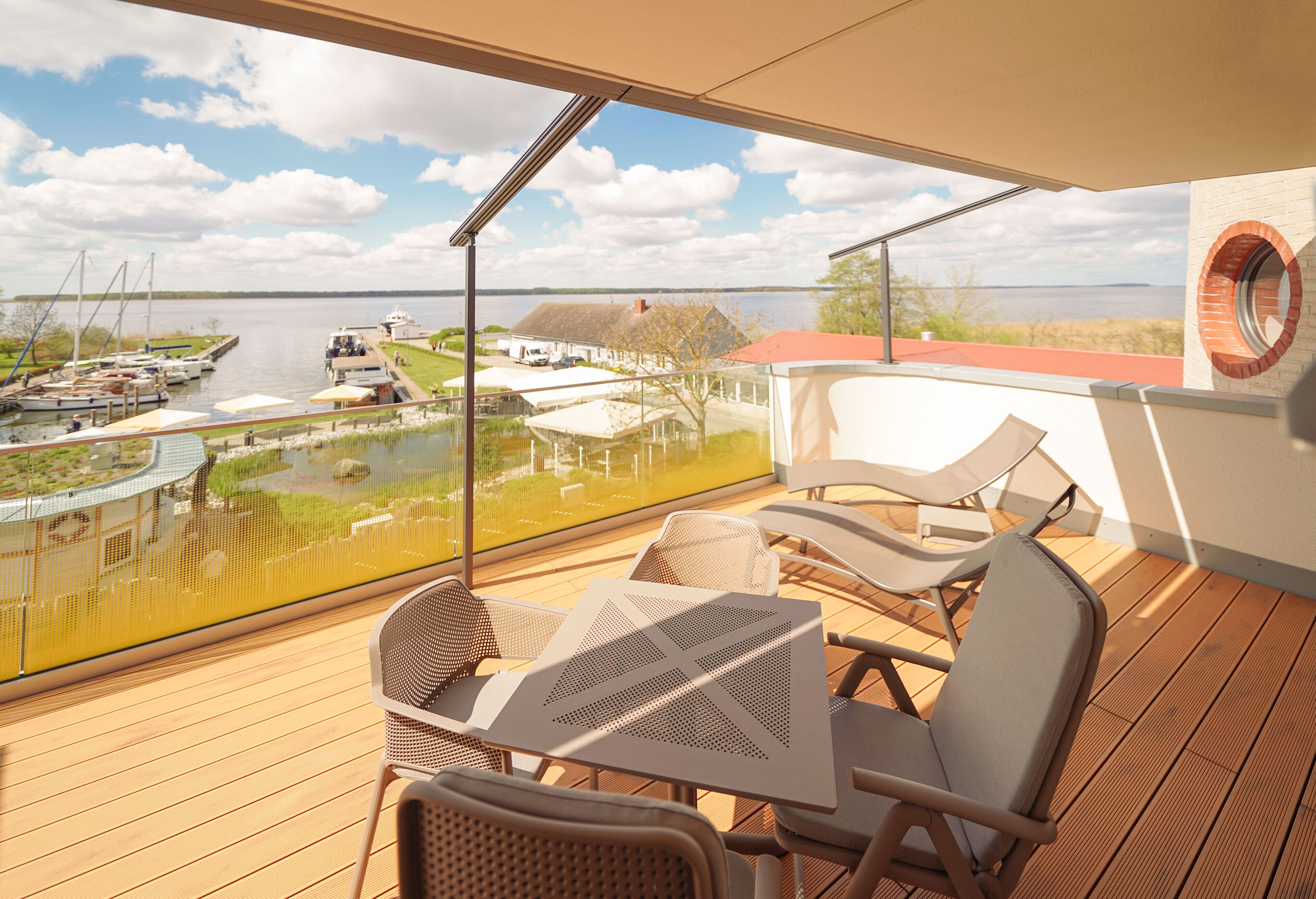 A balcony with a table and chairs, overlooking a marina with boats and a lake.