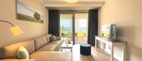 A modern living room with a sofa, a coffee table, a TV on a cabinet, and a view of the outdoors through a glass door.
