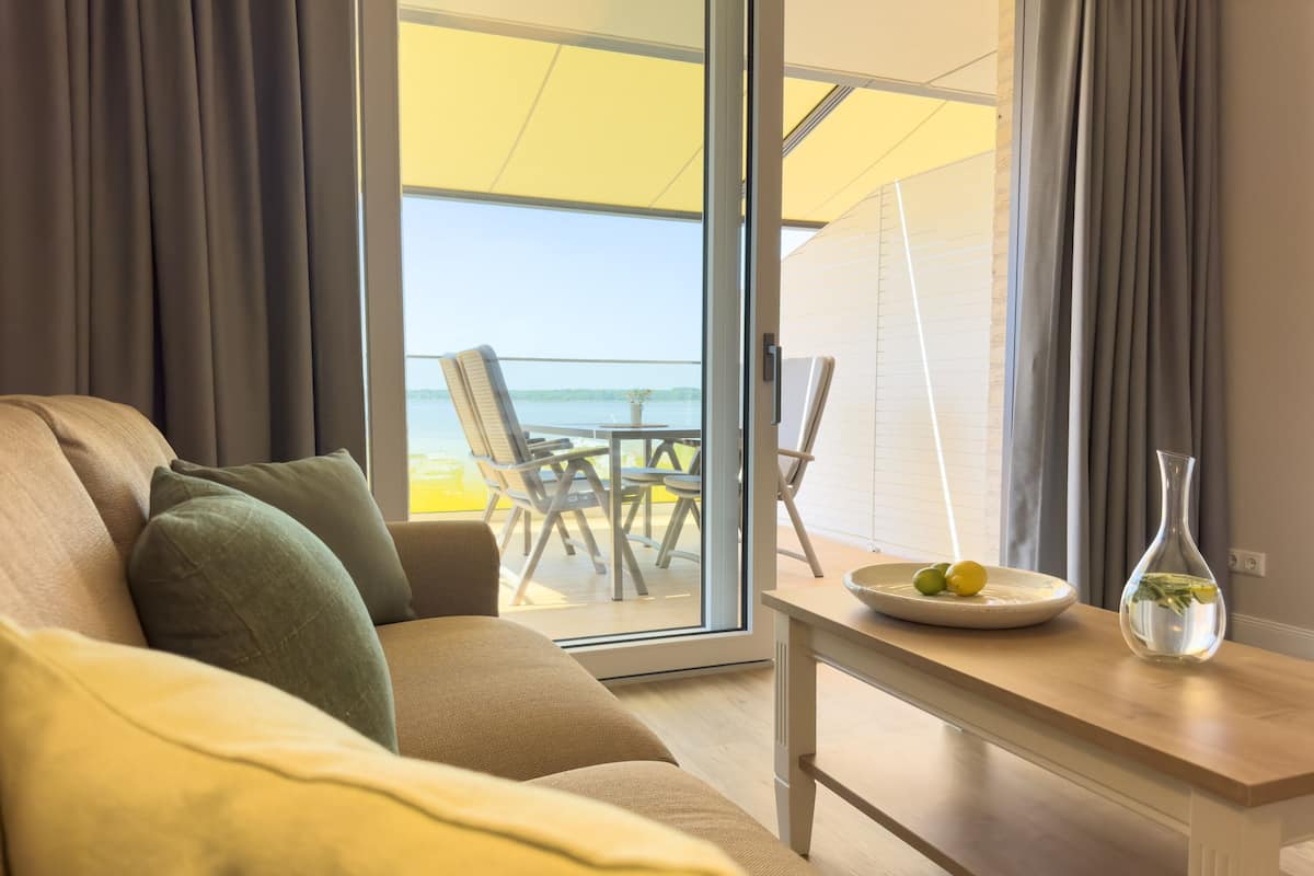 Un soggiorno moderno con un divano, un tavolo con un vaso e vista su un balcone con mobili da esterno.