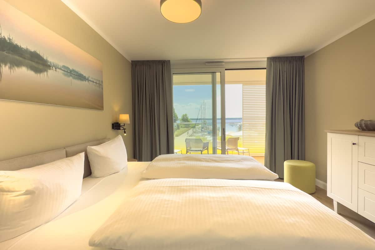 Camera d'albergo con un letto grande, vista sul mare, un balcone con sedie e un quadro appeso al muro.