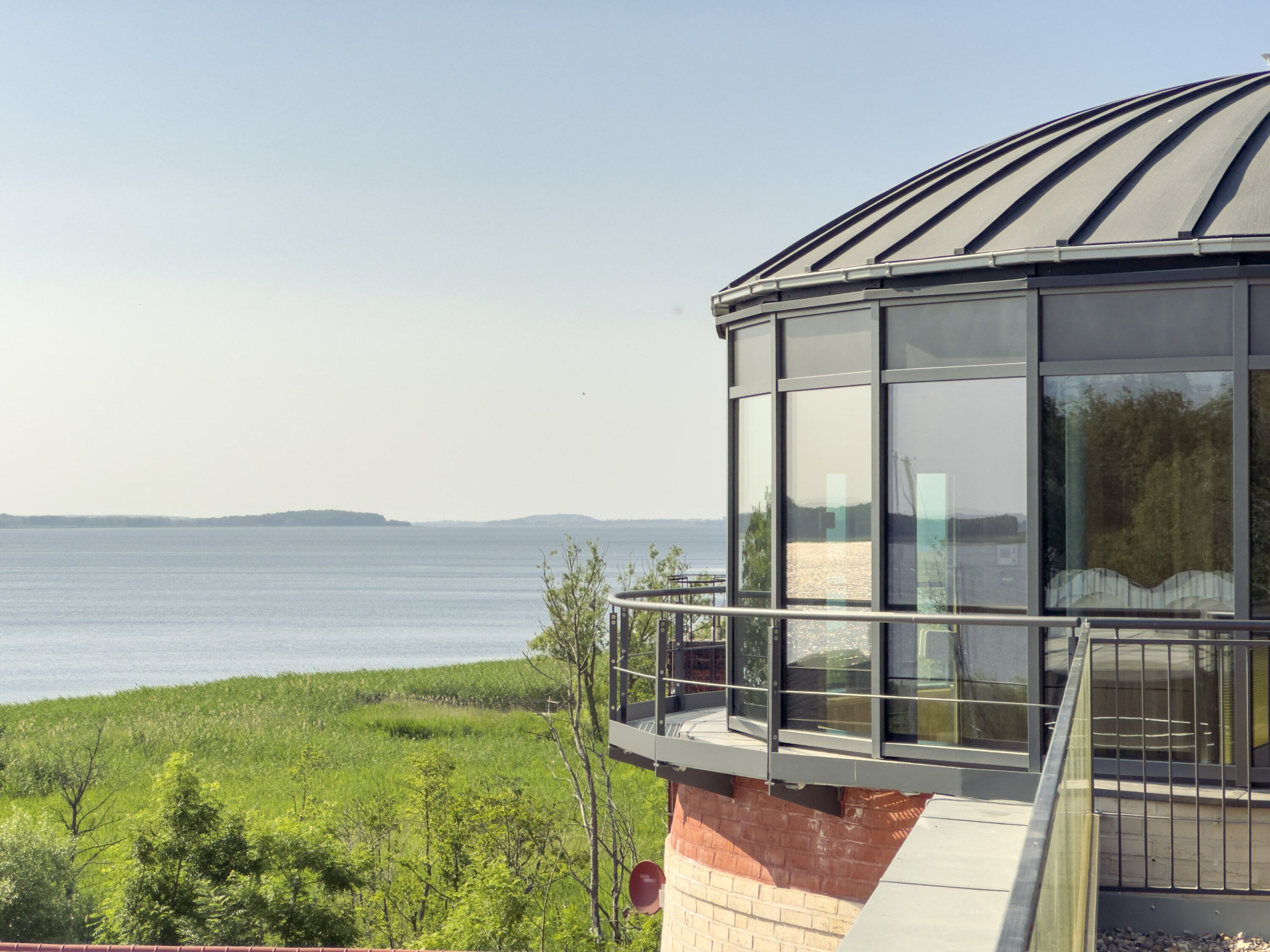 A modern building with large glass windows overlooking a body of water and greenery.