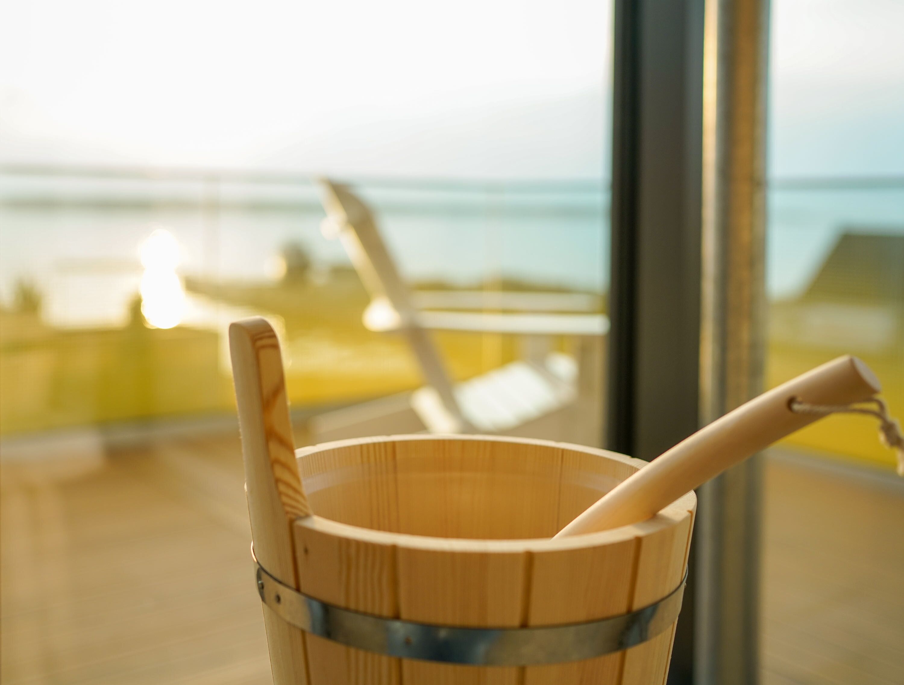 A wooden bucket with a wooden spoon inside, placed on a balcony with a view of the ocean.