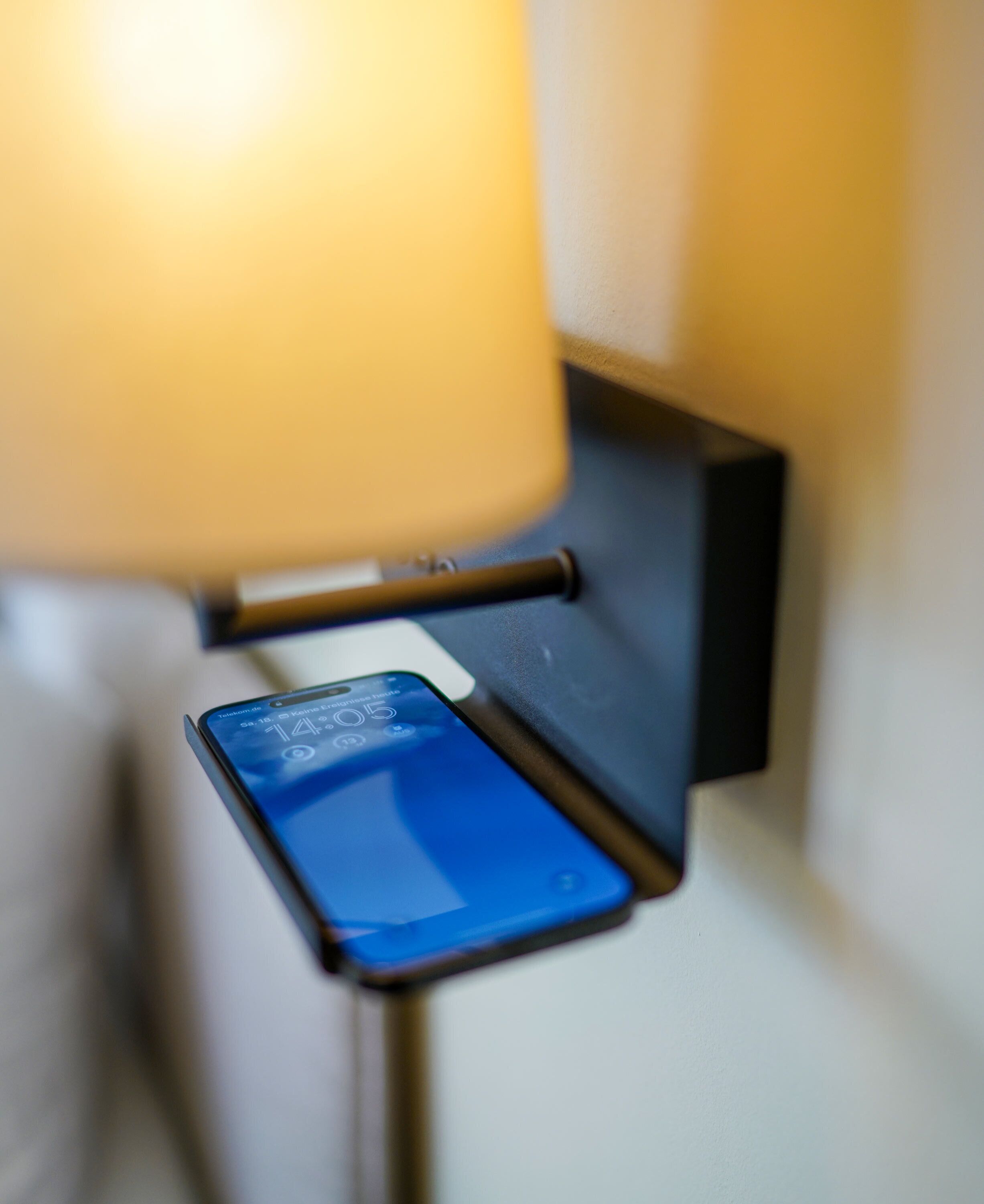 En smartphone som laddas på ett väggfäste bredvid en lampa.