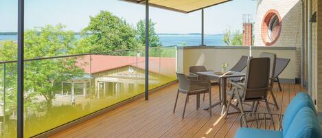 A balcony with a view of the sea, wooden flooring, and outdoor furniture including a table and chairs.