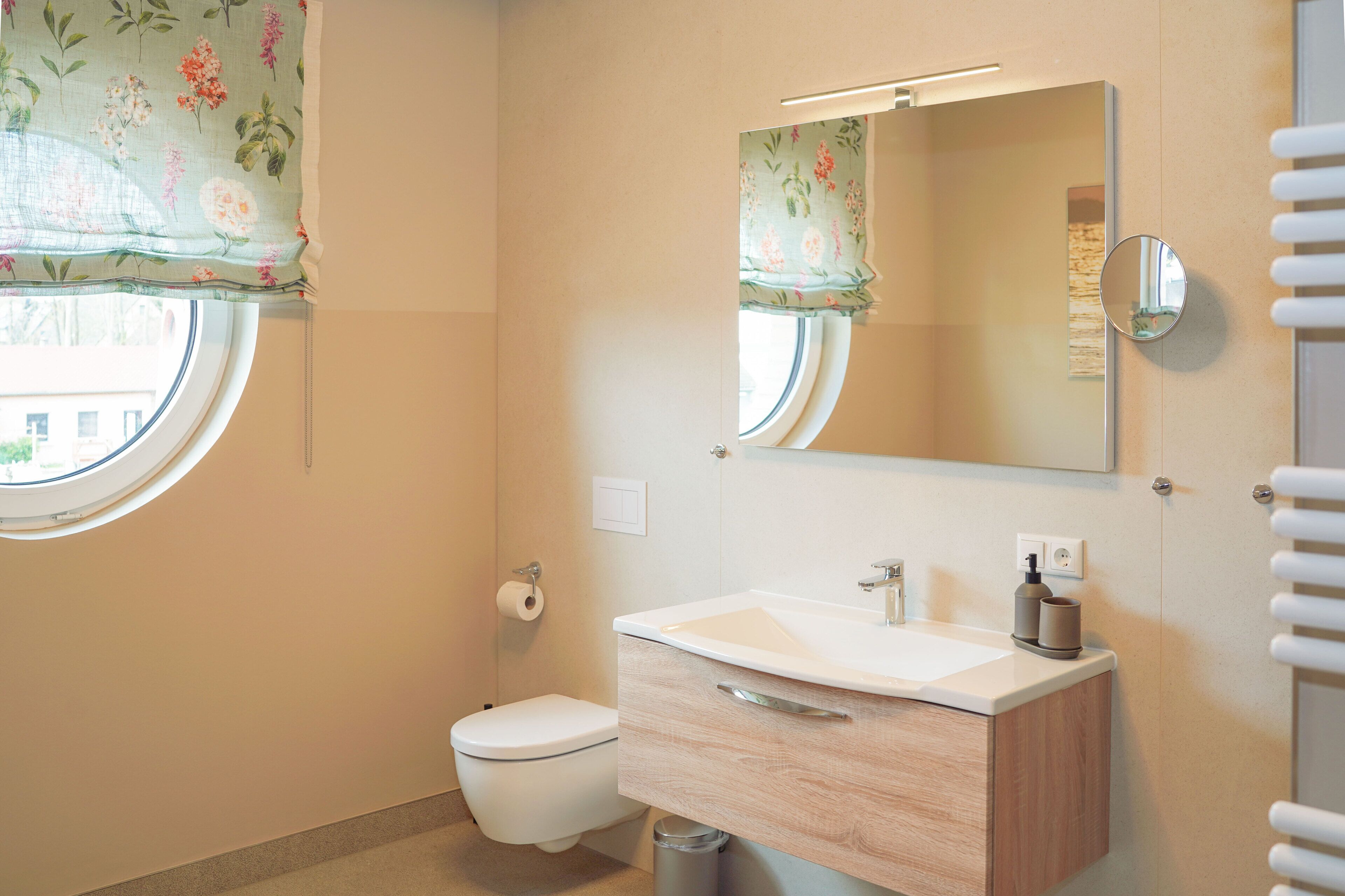A bathroom with a toilet, sink, mirror, and window with floral curtains.