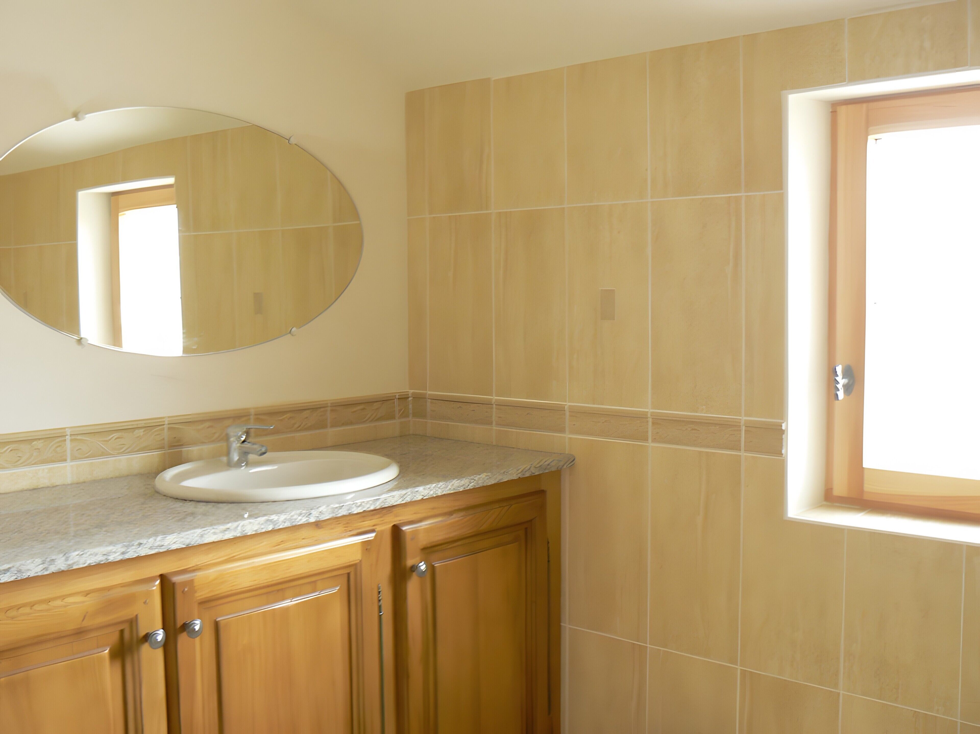 Une salle de bain avec un miroir rond, un lavabo, des meubles en bois et une fenêtre.