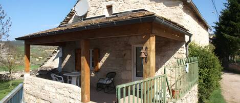 A stone house with a covered porch, a satellite dish, and a bell.