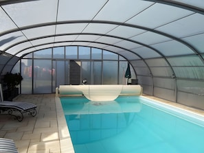 A covered swimming pool with a bench, a chair, and a potted plant.