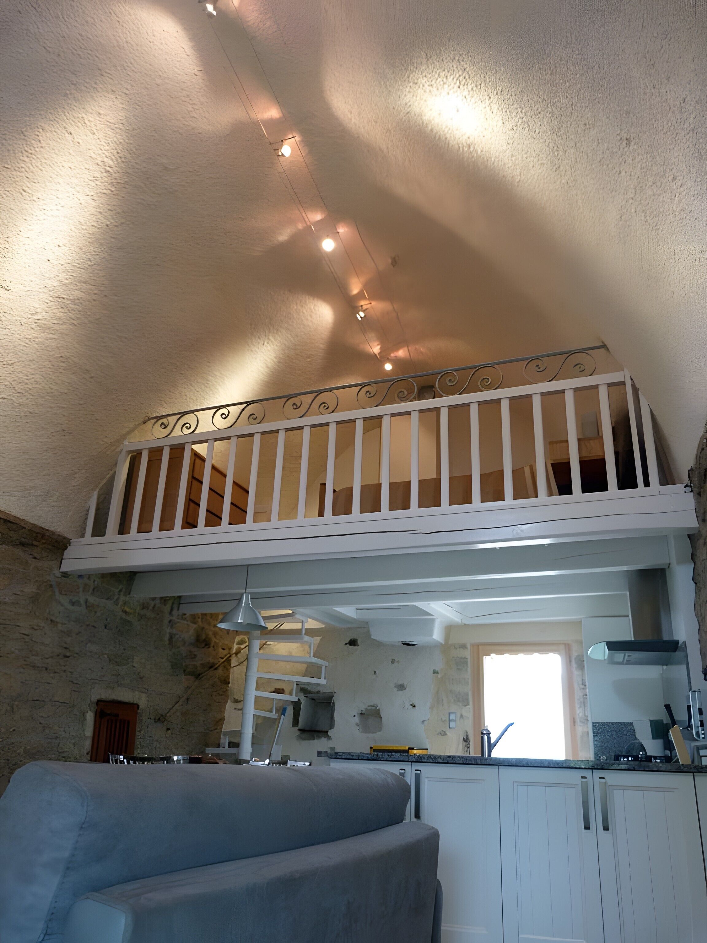 Eine Küche mit weißen Schränken, ein Essbereich mit einem blauen Sofa und ein Balkon mit einer weißen Brüstung.