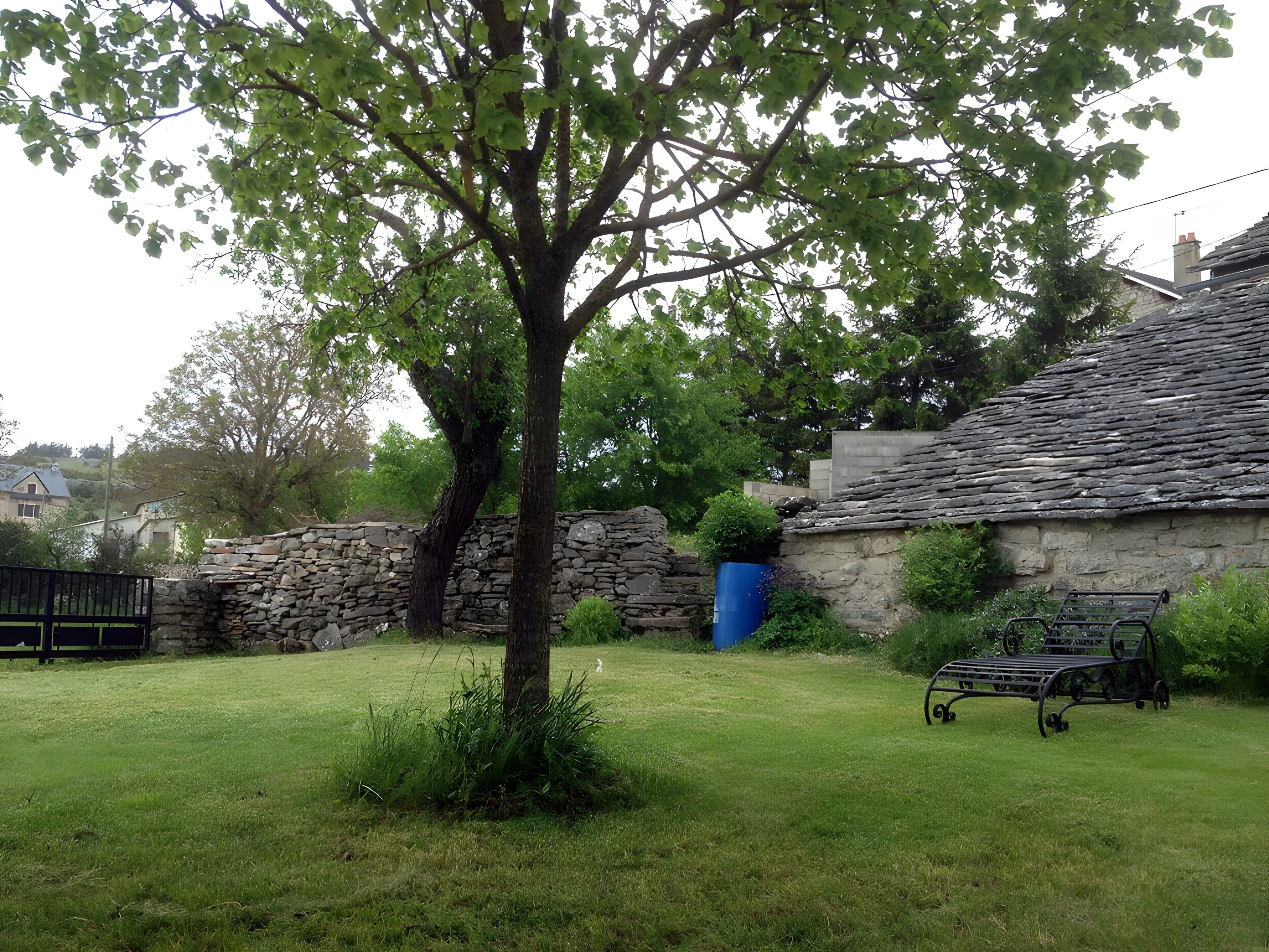 A stone building with a sloped roof, a tree in the foreground, and a metal bench.