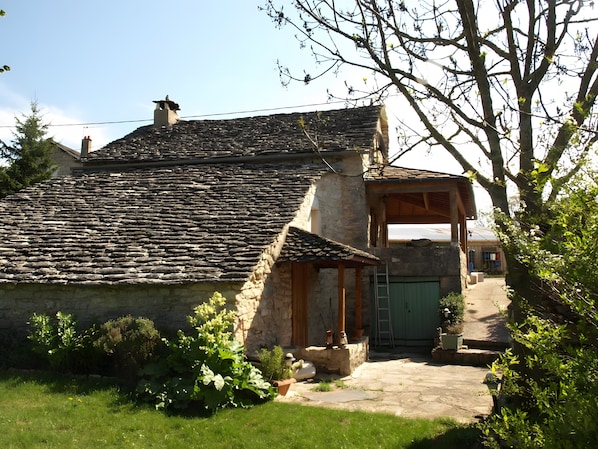 A stone house with a tiled roof, a wooden porch, and a green door.