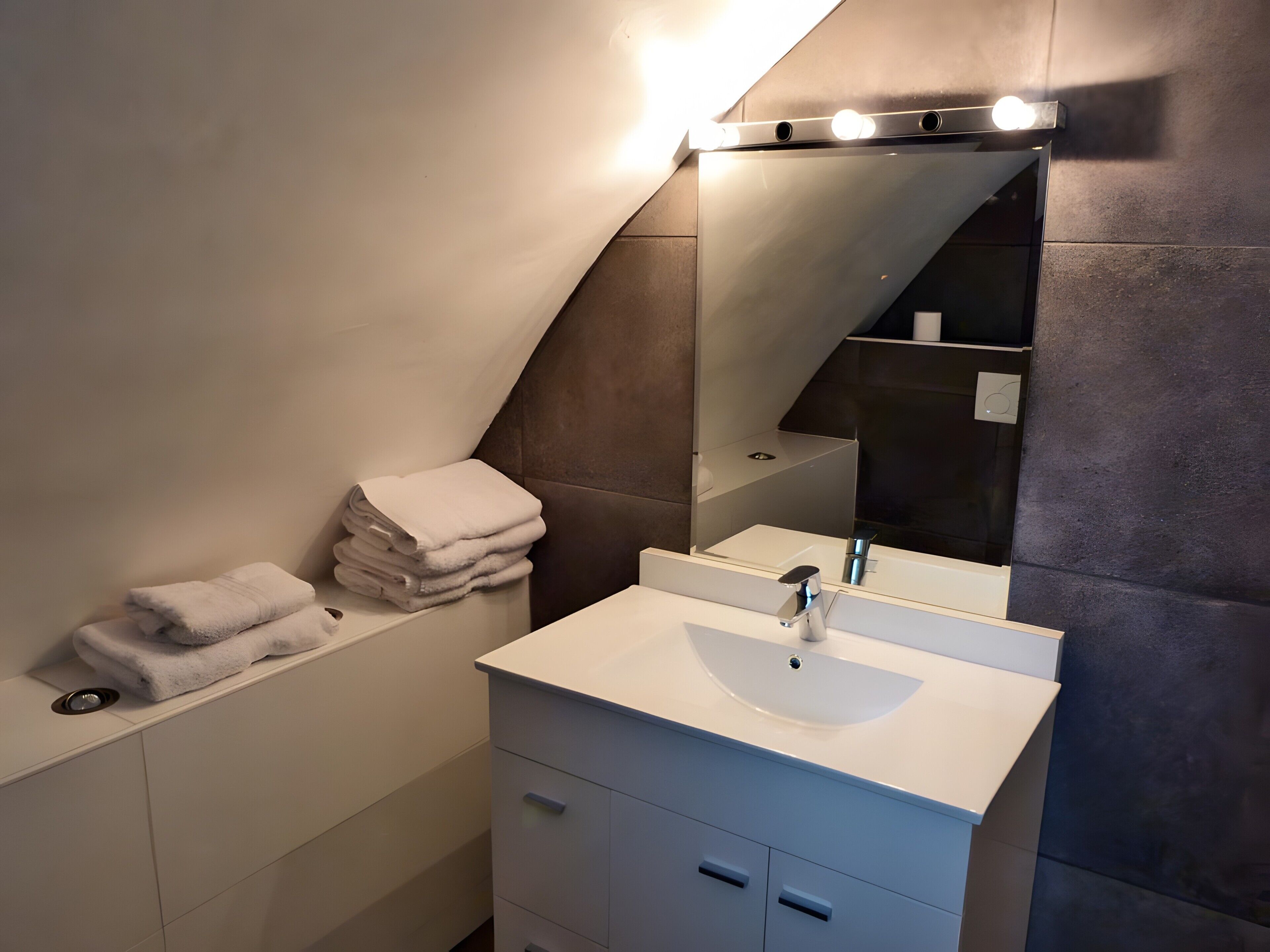 Une salle de bain moderne avec un lavabo blanc, un miroir et une pile d’essuie-serviettes.