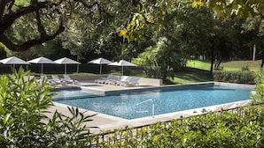 Une piscine rectangulaire entourée d’une végétation luxuriante, avec des chaises longues et des parasols.
