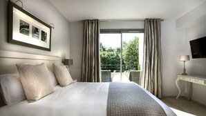 A hotel room with a large bed, a desk, a chair, a TV, and a balcony with curtains.