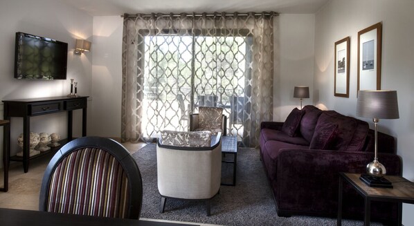 A living room with a television, a sofa, a chair, a table, and a window with curtains.