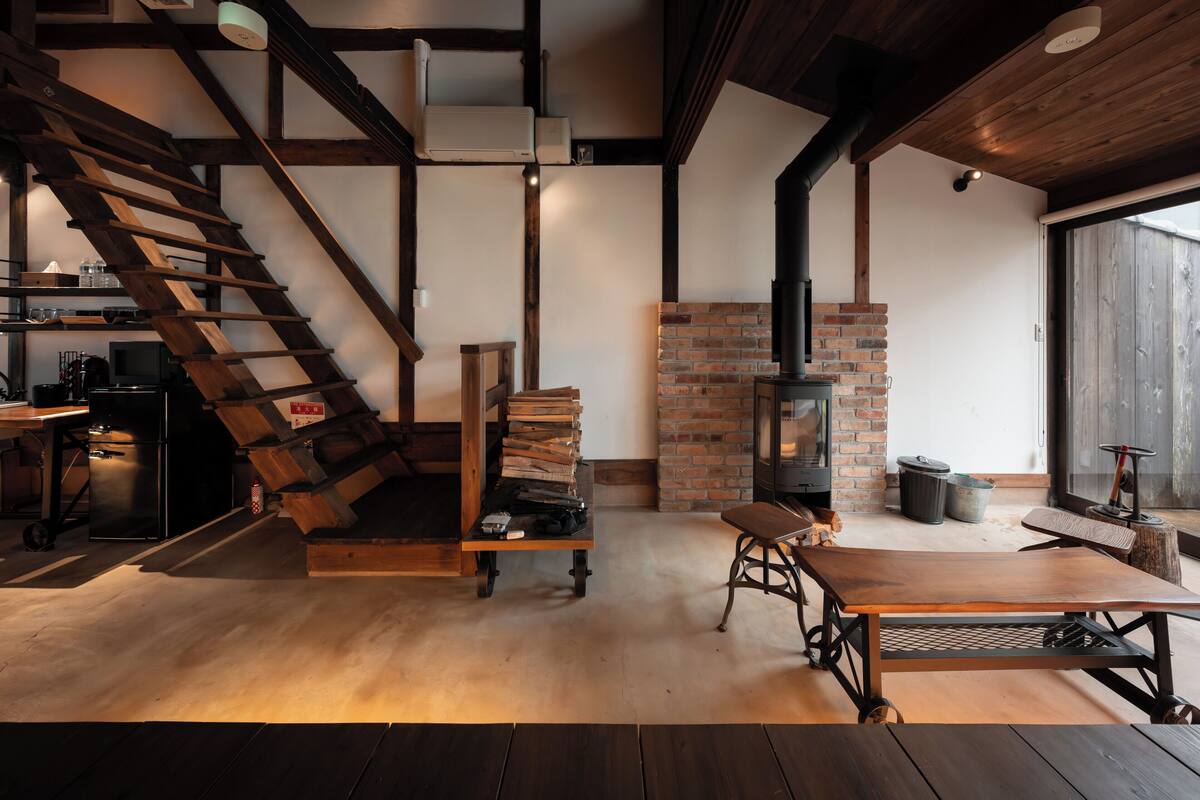 A rustic interior with a wooden staircase, a brick fireplace, and a dining area.
