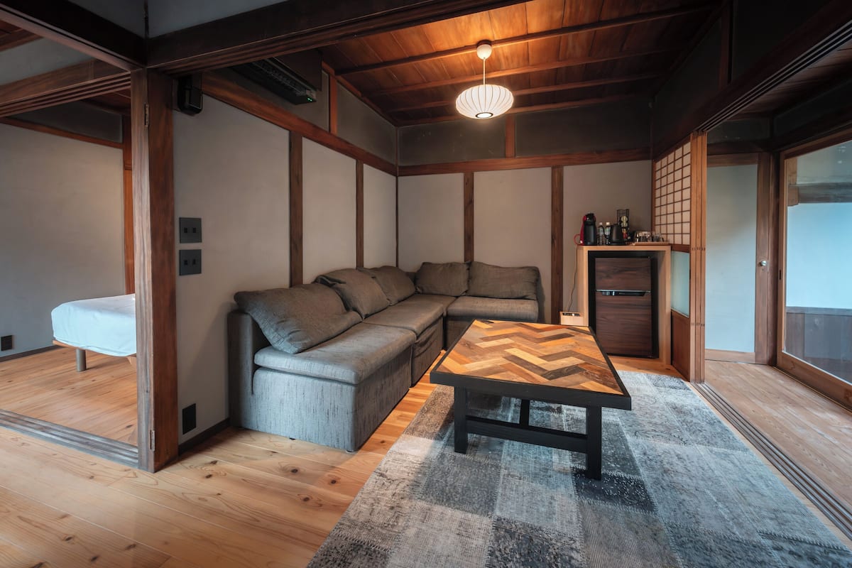 A modern living room with a sectional sofa, a herringbone-patterned coffee table, and a traditional Japanese sliding door.