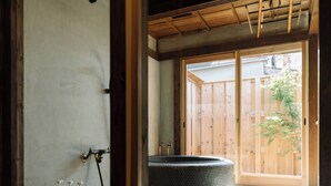 A traditional Japanese room with tatami flooring, a tatami mat seating area, and a sliding wooden door leading to a garden. - Kominka NOIE (Kushimoto)