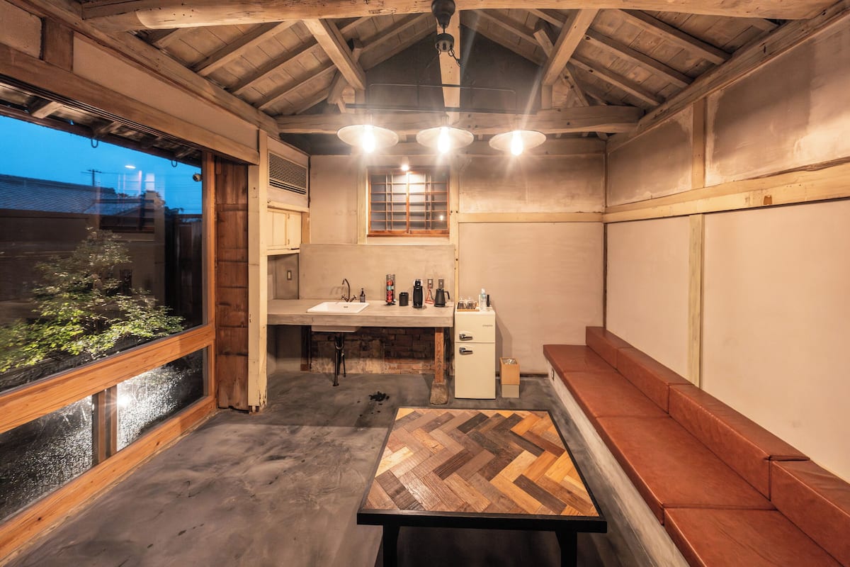 A rustic interior with a wooden ceiling, a large window, a sink, and a wooden table.