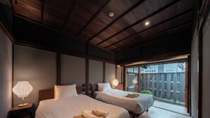 A hotel room with two beds, wooden flooring, and a view of a wooden fence through a glass door. - Kominka NOIE (Kushimoto)