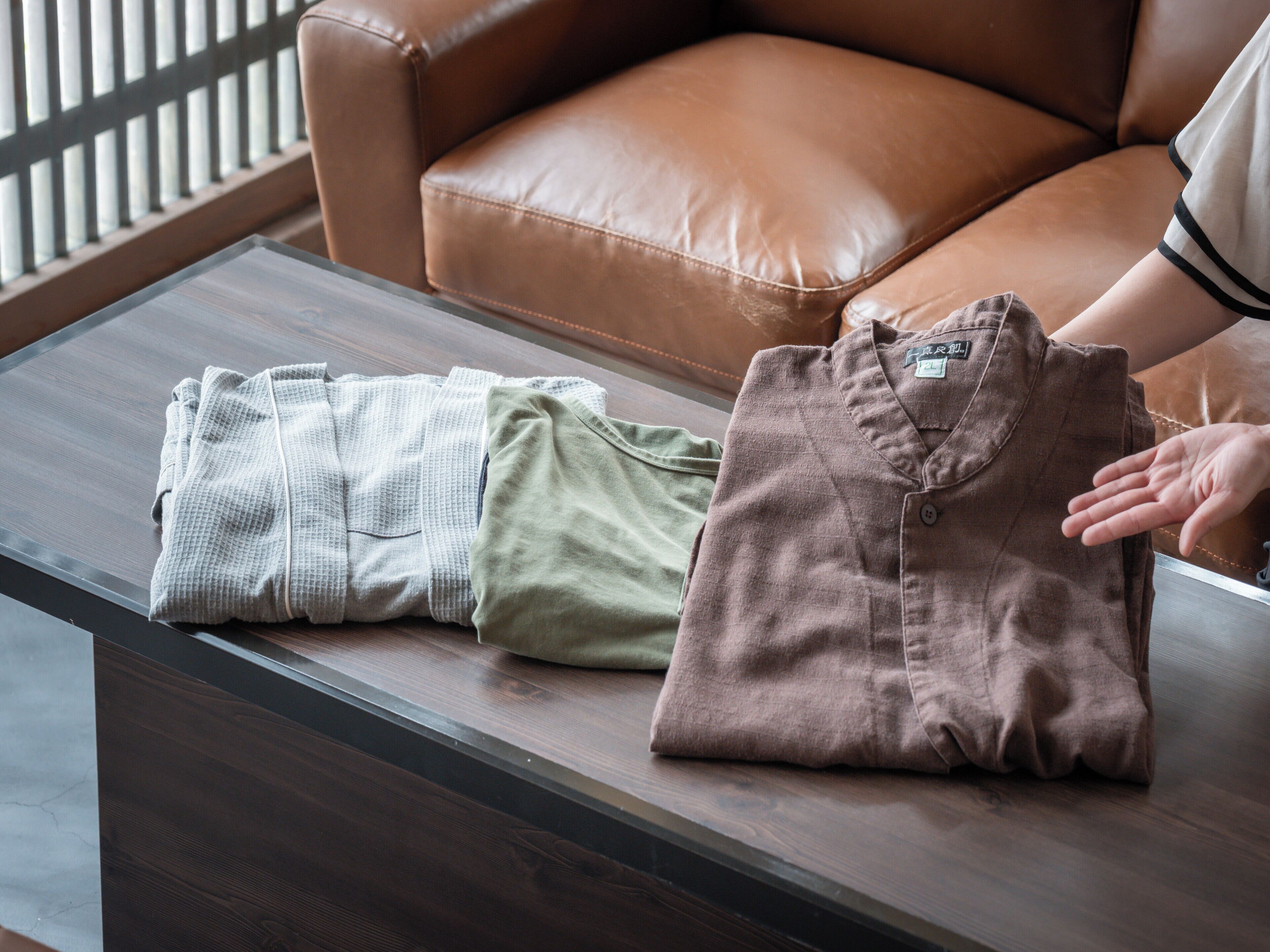A neatly folded brown shirt on a wooden table with a brown leather chair in the background.