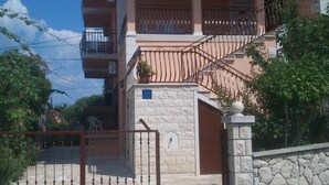 Edifício residencial com vários andares, fachada de pedra, entrada com portão e varandas com grades de metal.