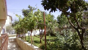 A stone-lined pathway with a metal fence on one side and a variety of trees and shrubs on the other. - Rooms Tatjana (Supetar)
