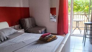 Quarto de hotel com cama, uma cadeira, uma mesinha e uma varanda com vista para o verde.
