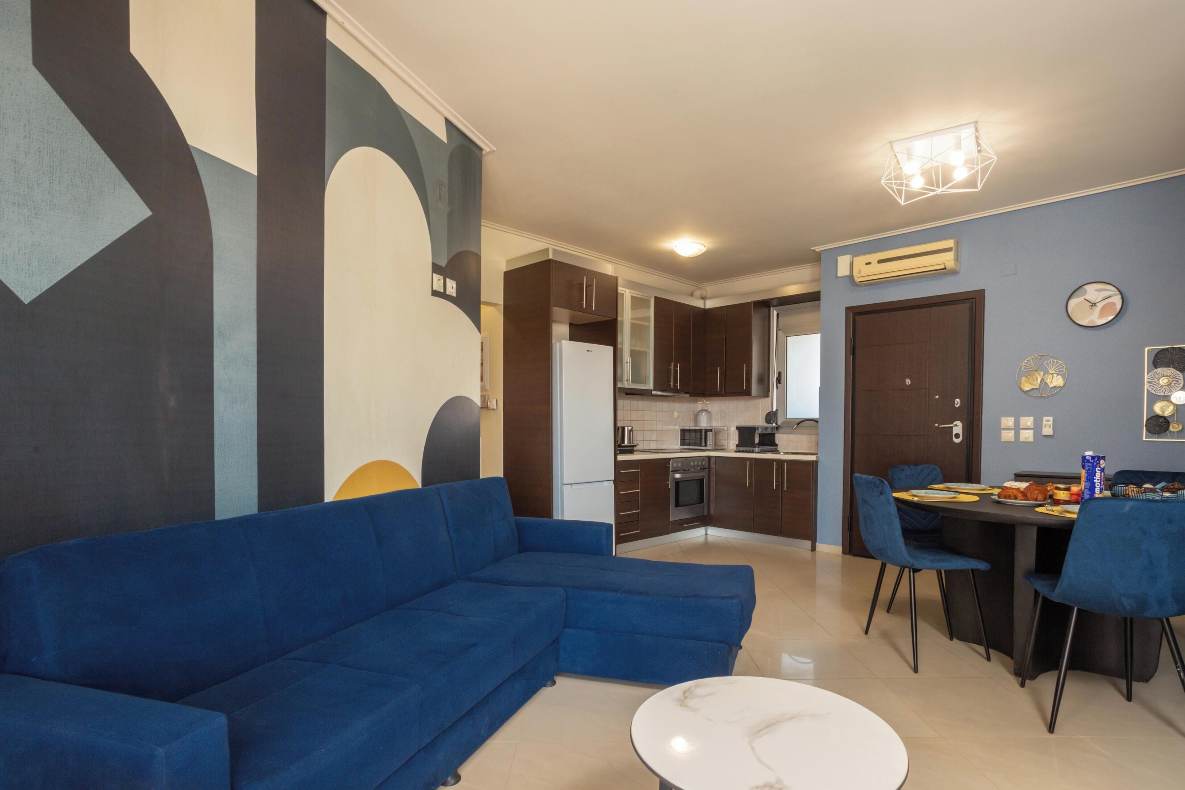 Un salon moderne avec un canapé bleu, une table à manger avec des chaises et un coin cuisine équipé de meubles et d’appareils électroménagers.