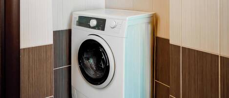 A compact laundry room with a front-loading washing machine, wooden panel walls, and dark brown tiled flooring.