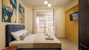A bedroom with a large bed, a TV on the wall, and a view of the outside balcony. - Zen City Beach Apartment (Chania)