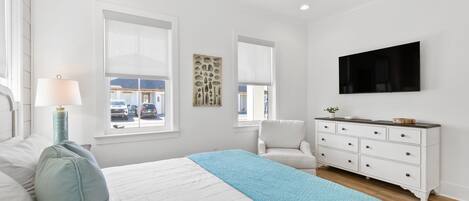 A bedroom with a bed, a dresser, a chair, a ceiling fan, and a TV on the wall.