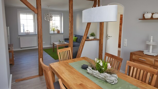 Ein Essbereich mit Holztisch, Stühlen, einer Hängeleuchte und Blick in das Wohnzimmer.
