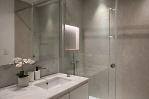Ein modernes Badezimmer mit Duschkabine aus Glas, Marmorwaschbecken und einer Topf-Orchidee.