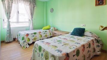 Una habitación con dos camas, una ventana con cortinas, un reloj y un cuadro pequeño en la pared.