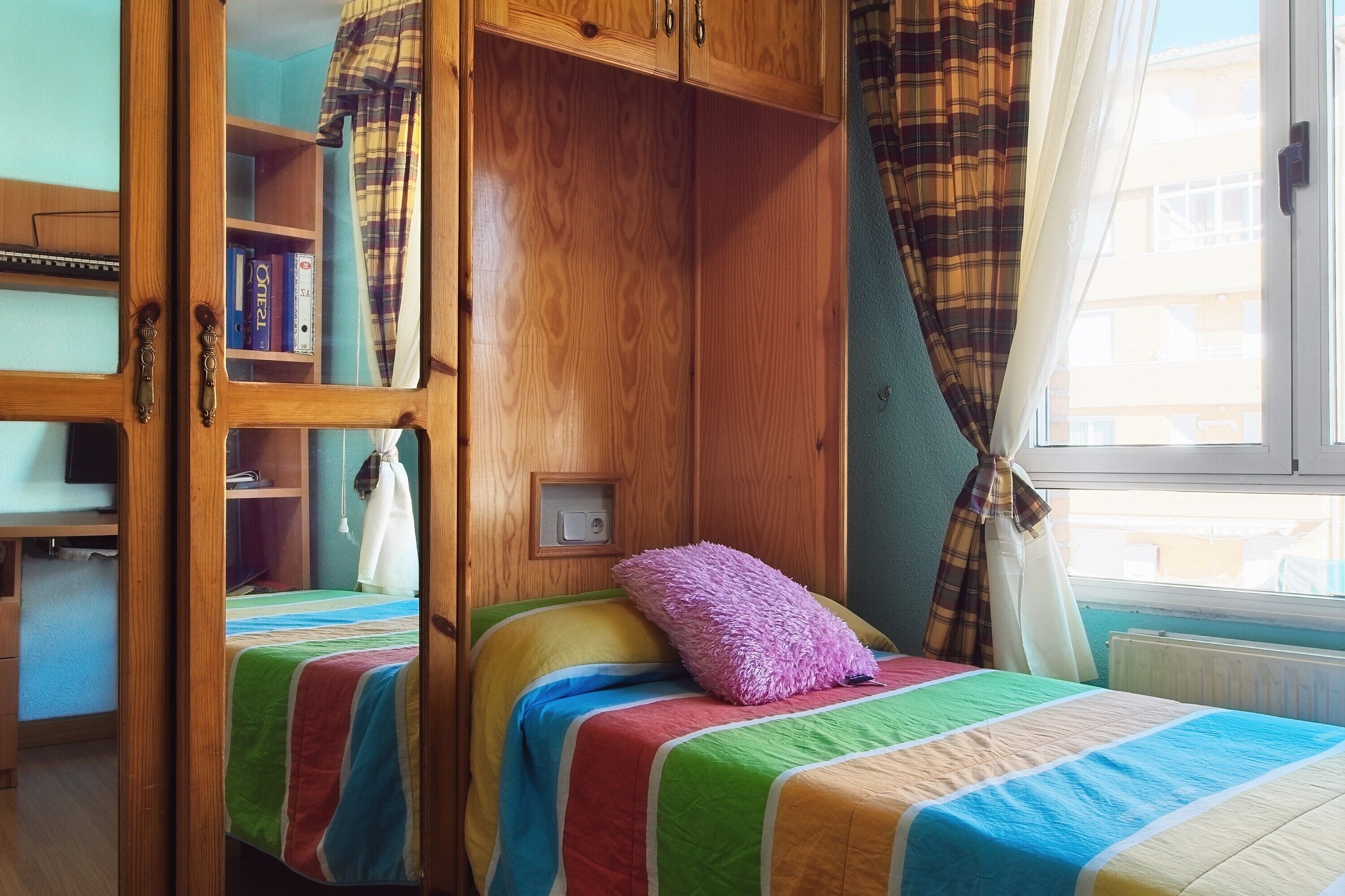 Un dormitorio con cama, armario y ventana con cortinas.