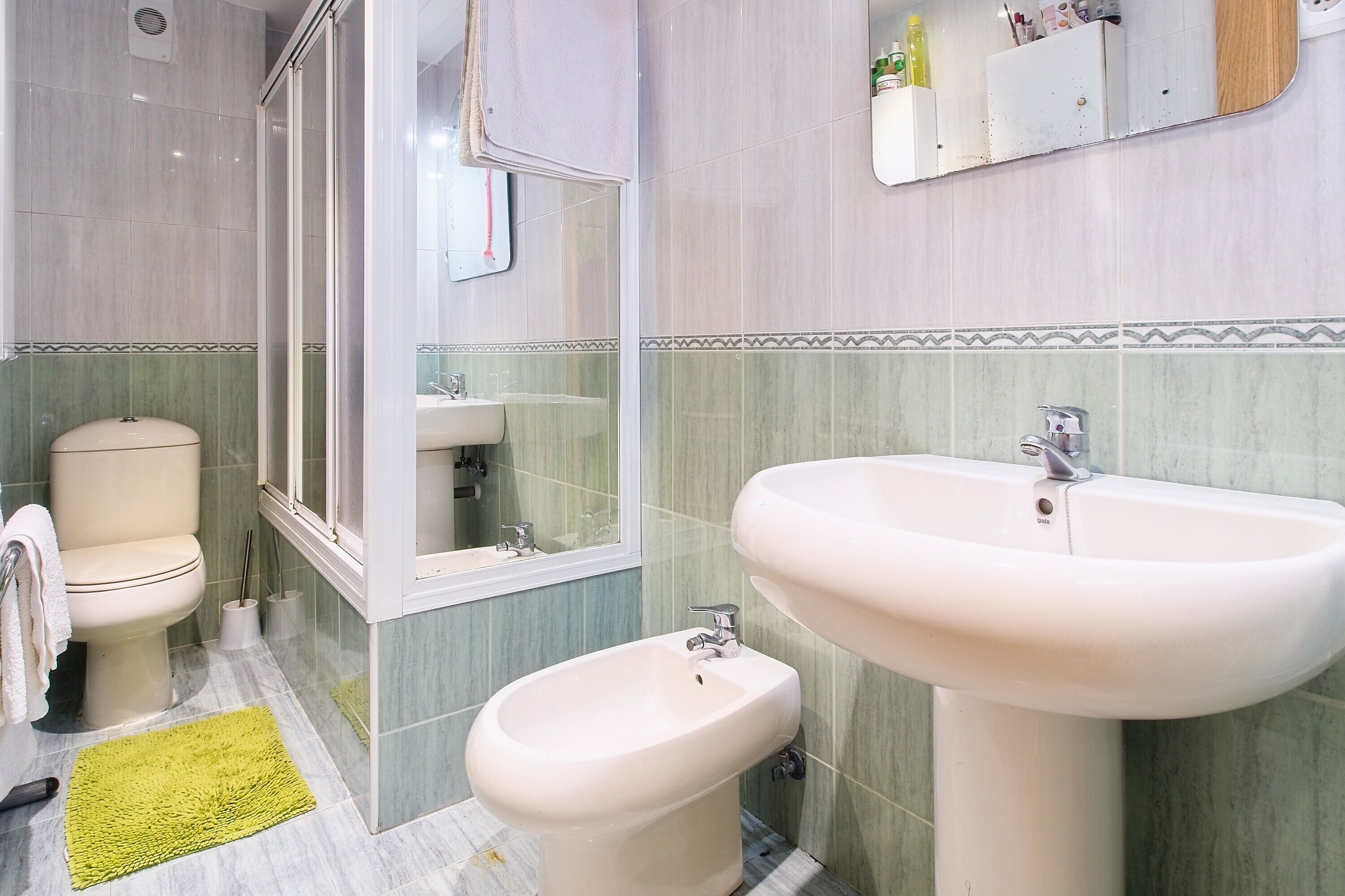 Een badkamer met toilet, bidet, wastafel, spiegel en groene tegels.