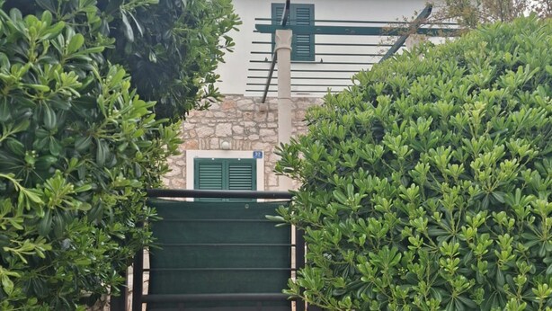 A gated entrance with a metal gate, surrounded by lush green shrubs and a stone wall. - Villa Jagoda (Orebic)