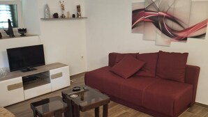 A living room with a red sofa, a glass coffee table, a TV on a wooden stand, and a wall with abstract art. - Villa Jagoda (Orebic)