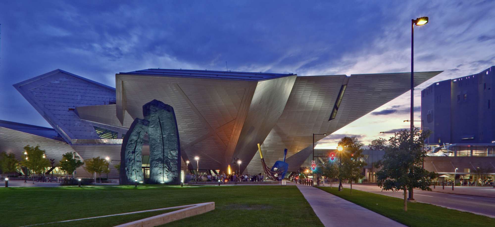 A modern building with a unique angular design, featuring a prominent central sculpture and a spacious outdoor area with a pathway.