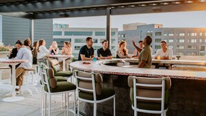 Eine Dachterrasse mit Außenbestuhlung, einer Bar und Blick auf moderne Gebäude.