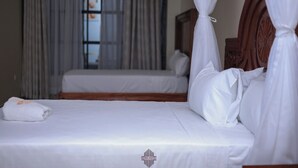 Een hotelkamer met twee bedden, een houten hoofdeinde en een raam met gordijnen.