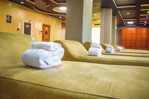 A row of neatly made beds with towels, a wooden door, and a wall with lockers.